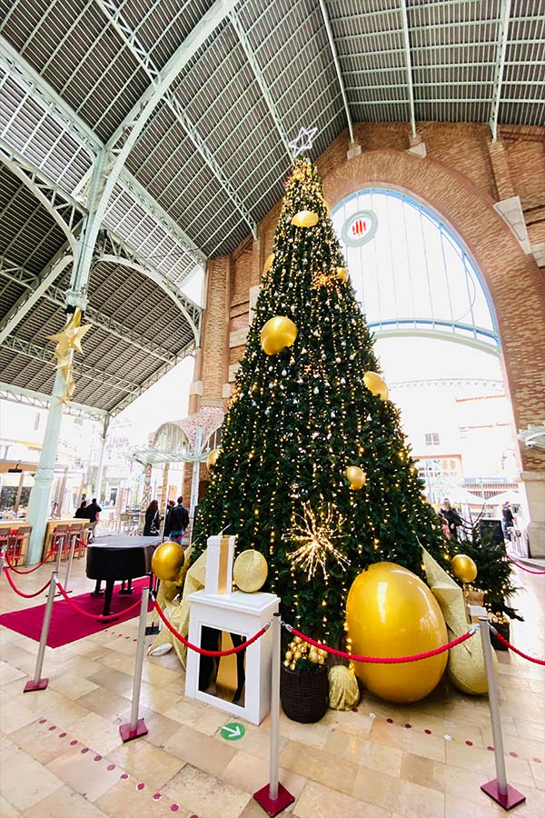 tree in mercat colon valencia with white piano to the left rear and golden balls by tree during the christmas season in valencia