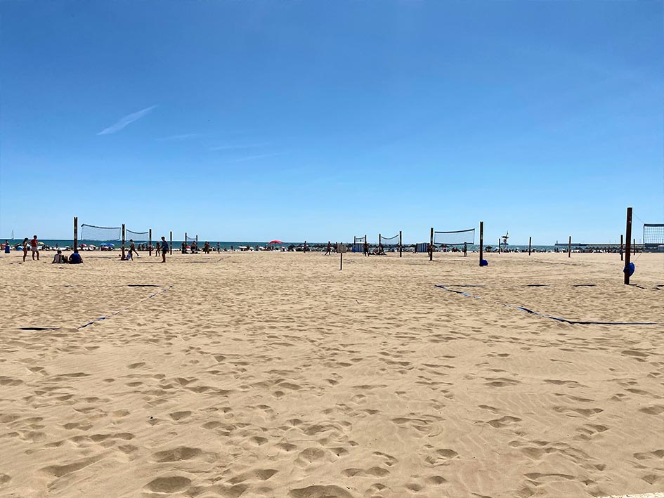 Malvarossa beach in Valencia with sand and people playing volleyball. All about living in Valencia versus visiting.